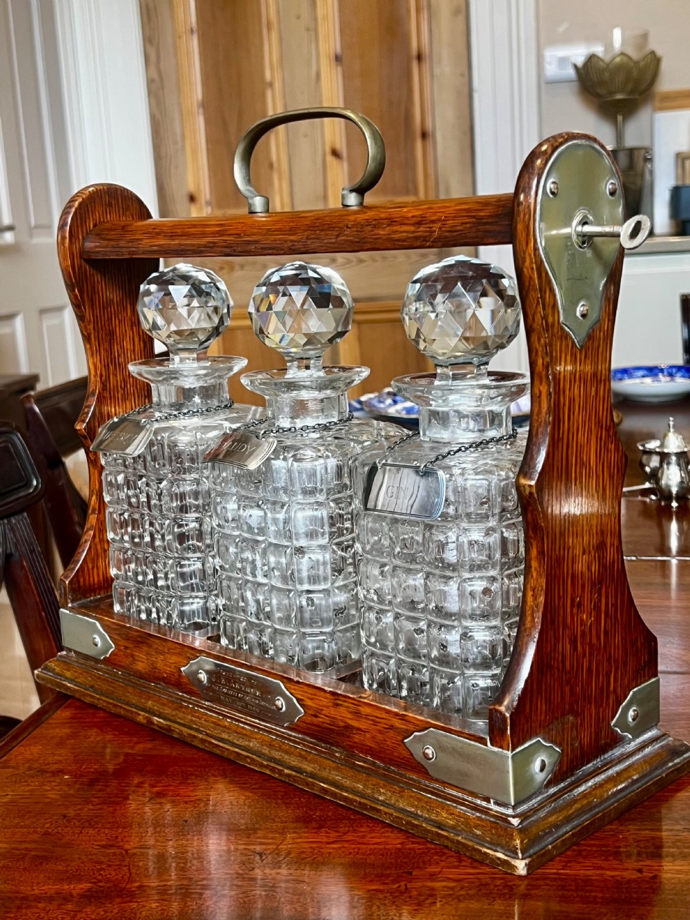 An antique Edwardian oak tantalus housing three cut-glass decanters with matching silver labels, fitted with a brass handle and locking mechanism.