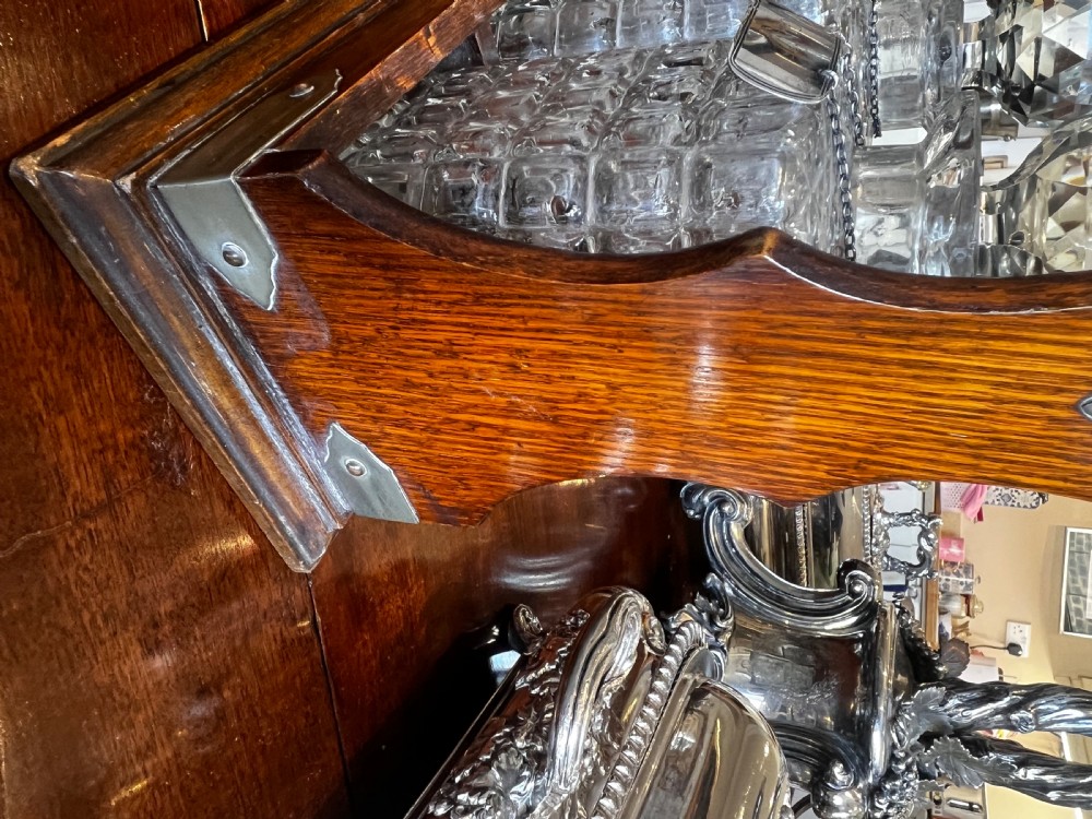 An antique Edwardian oak tantalus housing three cut-glass decanters with matching silver labels, fitted with a brass handle and locking mechanism. View IV