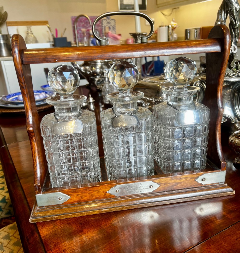 An antique Edwardian oak tantalus housing three cut-glass decanters with matching silver labels, fitted with a brass handle and locking mechanism. View IX