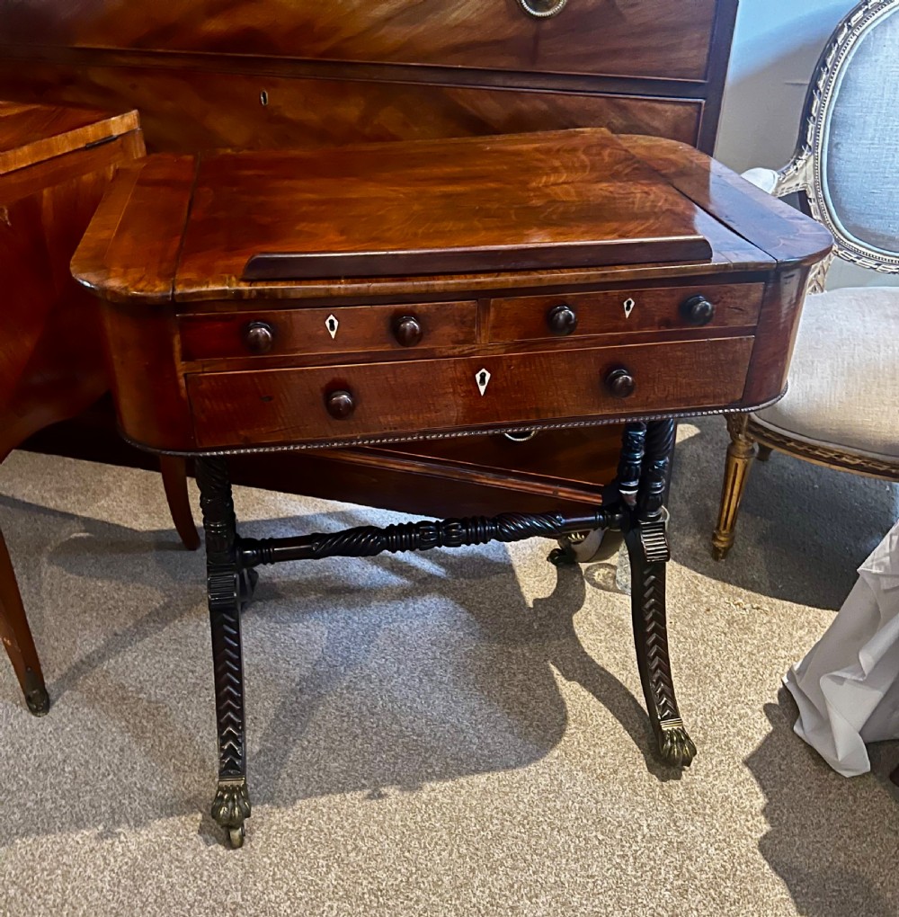 An antique dark wood Regency reading table featuring an adjustable sloped top, small drawers with brass key escutcheons, and carved intersecting legs with castors. View II