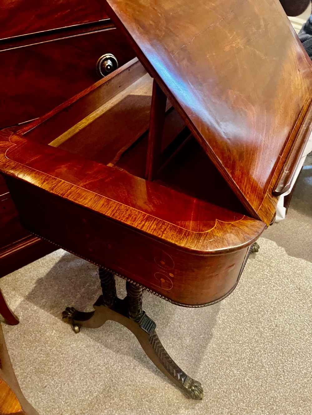 An antique dark wood Regency reading table featuring an adjustable sloped top, small drawers with brass key escutcheons, and carved intersecting legs with castors. View IV