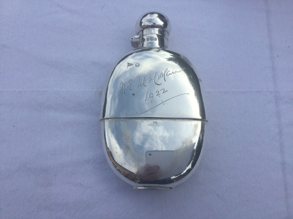 A curved silver hip flask featuring an engraved signature dated 1922, hallmarked collar, and a hinged domed cap.