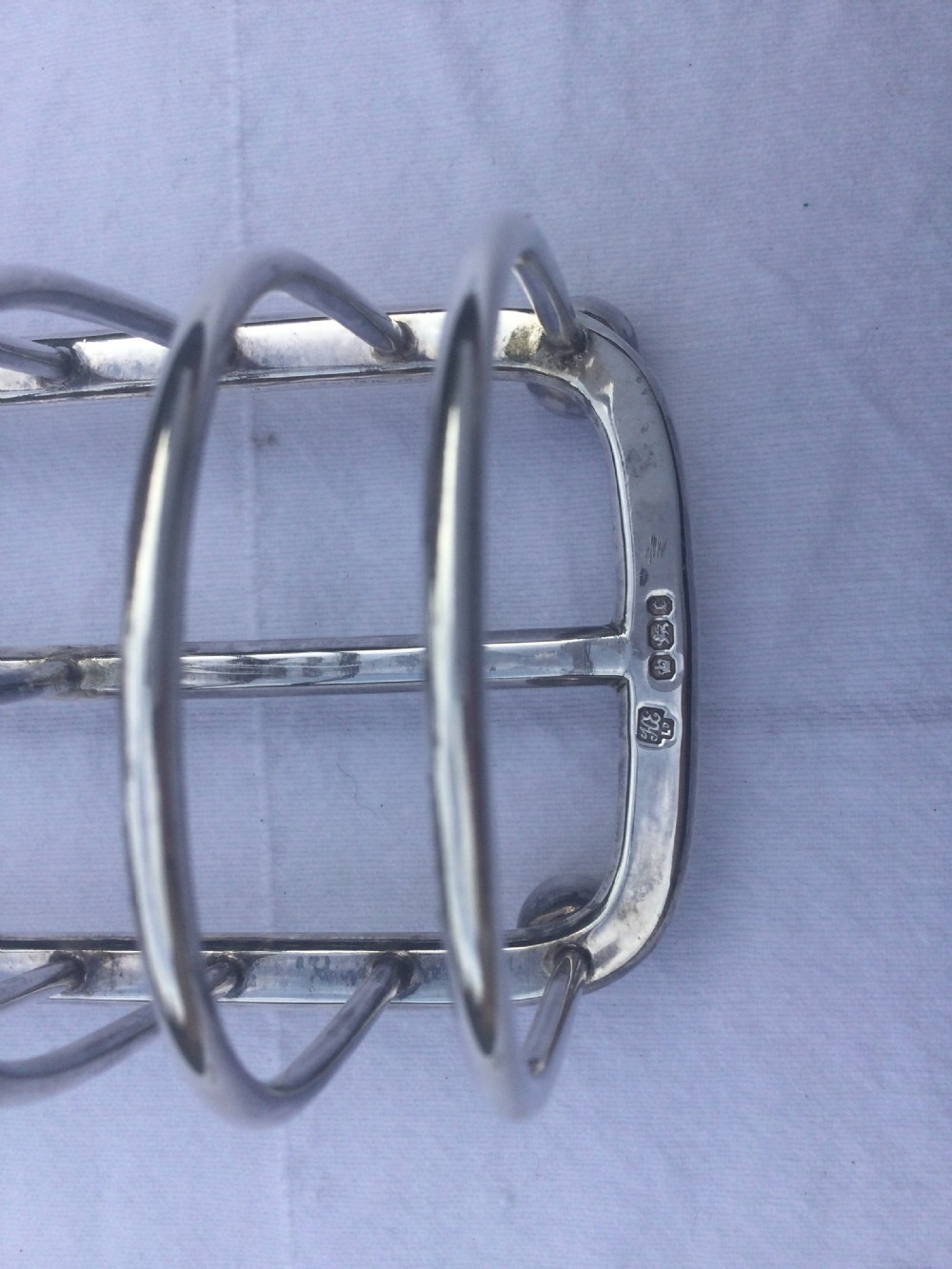 A silver six-slot toast rack featuring arched wire dividers, a central oval loop handle, and four small ball feet resting on a plain background. View IV