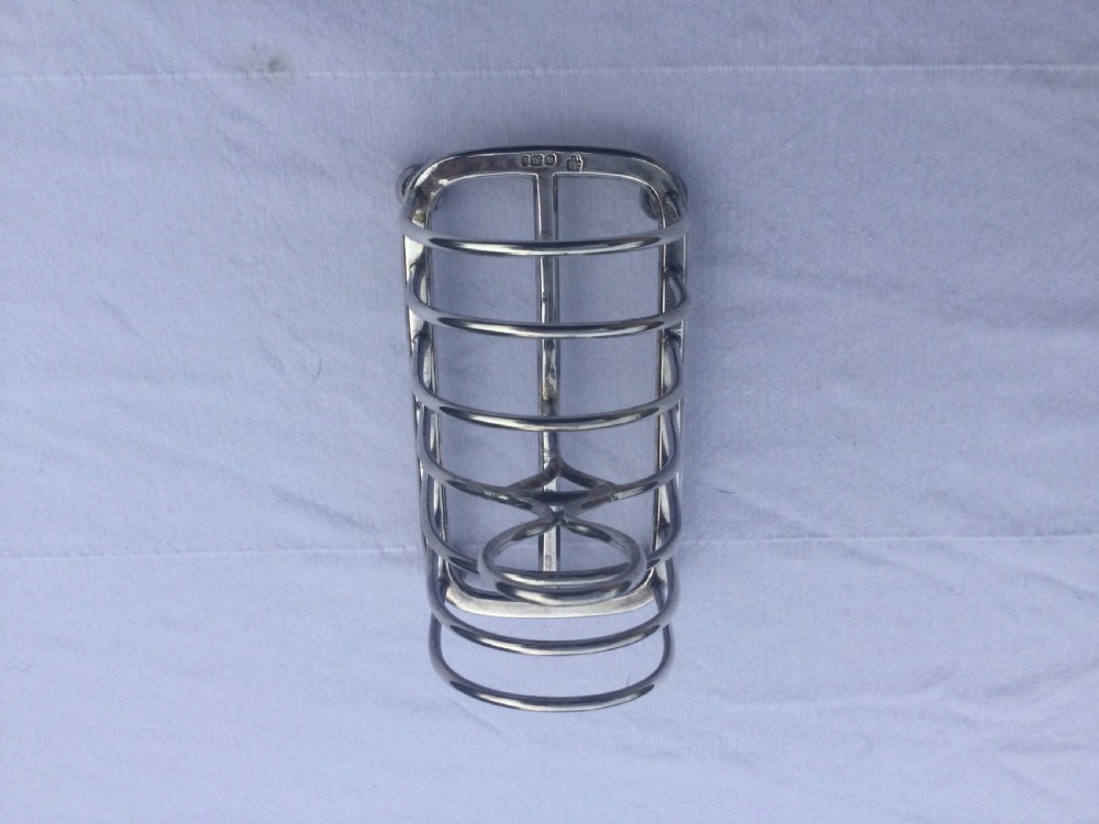 A silver six-slot toast rack featuring arched wire dividers, a central oval loop handle, and four small ball feet resting on a plain background. View VI