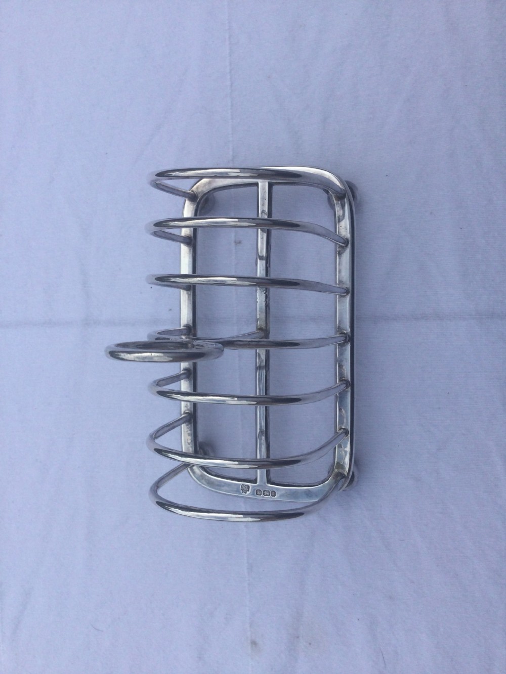 A silver six-slot toast rack featuring arched wire dividers, a central oval loop handle, and four small ball feet resting on a plain background. View VIII