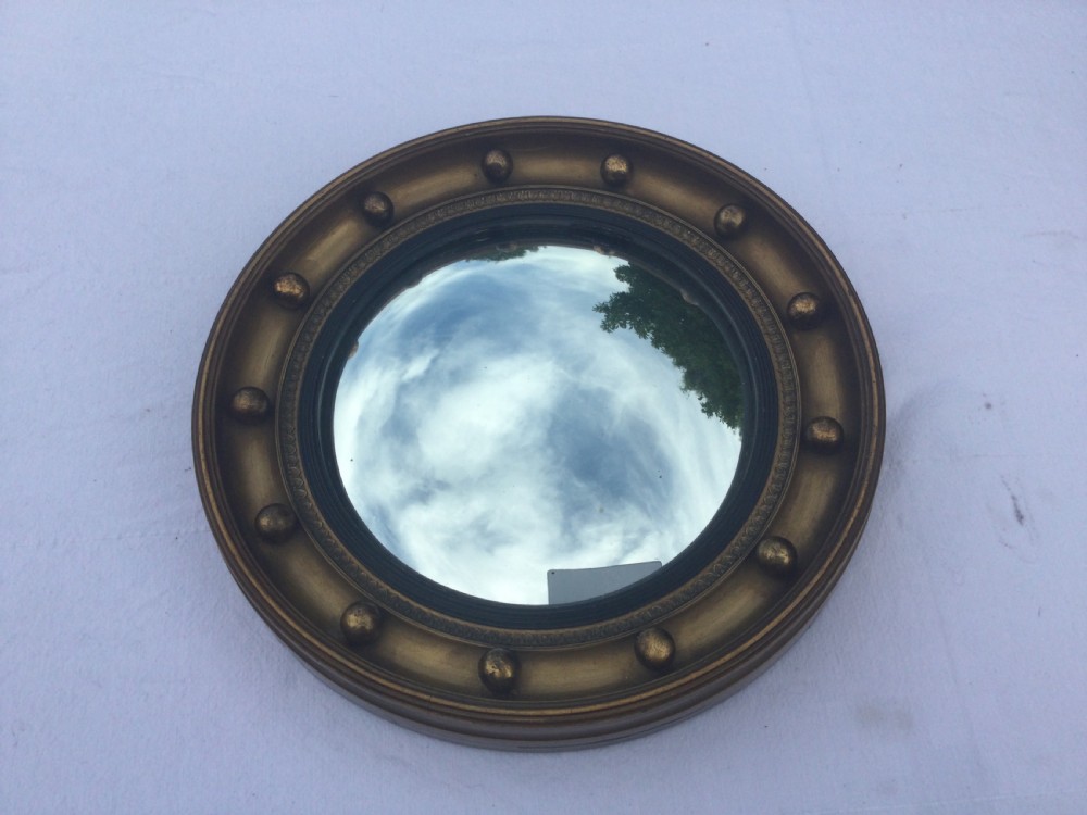 A circular Regency style convex wall mirror featuring a gilded frame decorated with evenly spaced ball ornaments around the cavetto moulding.