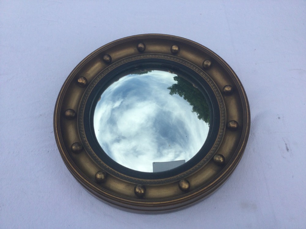 A circular Regency style convex wall mirror featuring a gilded frame decorated with evenly spaced ball ornaments around the cavetto moulding. View II