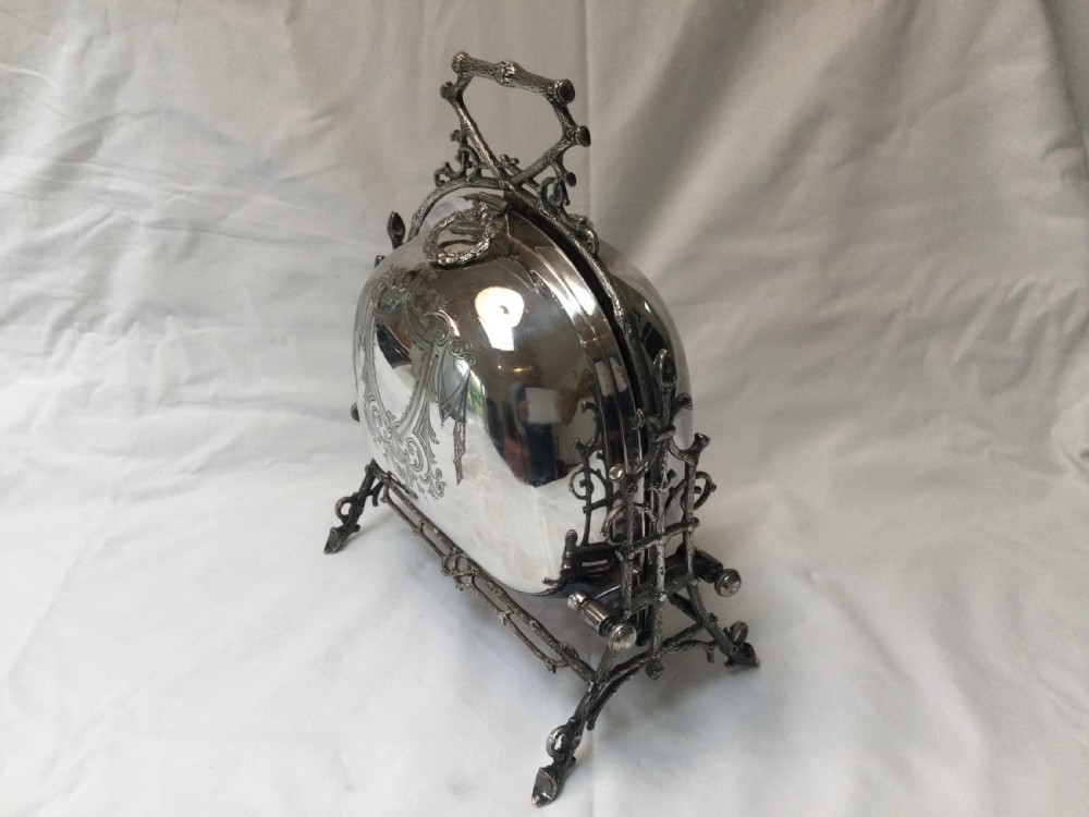 A Victorian silver-plated revolving biscuit barrel featuring engraved foliage patterns, mounted within an ornate cast twig-form metal stand. View II