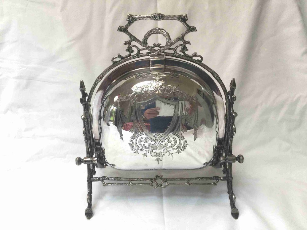 A Victorian silver-plated revolving biscuit barrel featuring engraved foliage patterns, mounted within an ornate cast twig-form metal stand.
