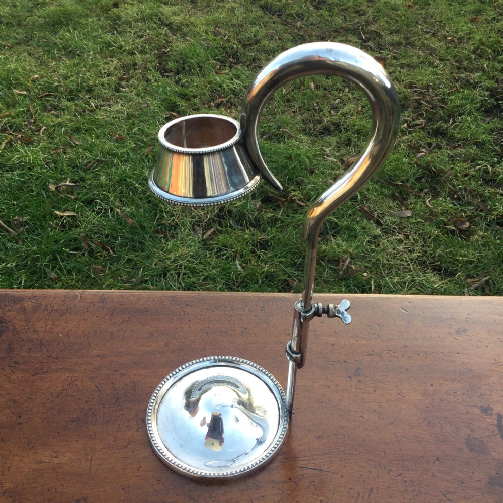 An adjustable silver-plated champagne bottle holder featuring a circular base with a beaded rim, a vertical support rod with a wing nut adjustment, and a top collar.