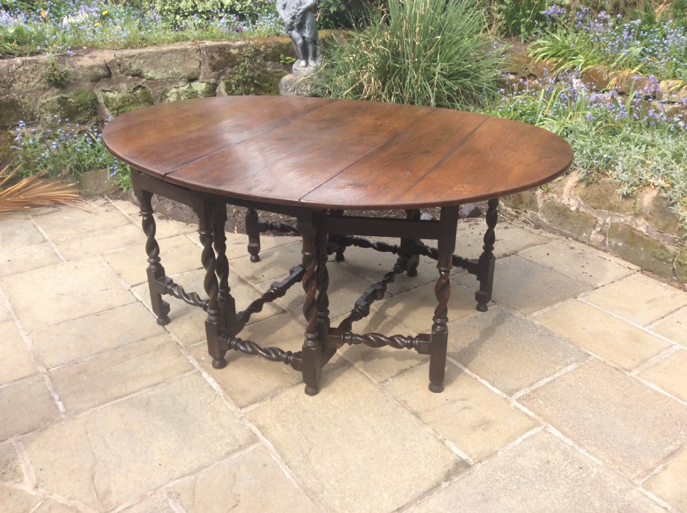 An antique dark oak oval gateleg table featuring barley twist turned legs, stretchers, and folding drop leaves.