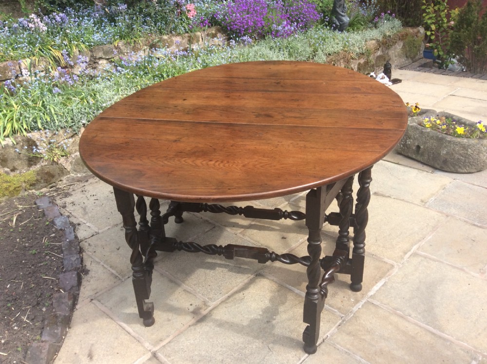 An antique dark oak oval gateleg table featuring barley twist turned legs, stretchers, and folding drop leaves. View II