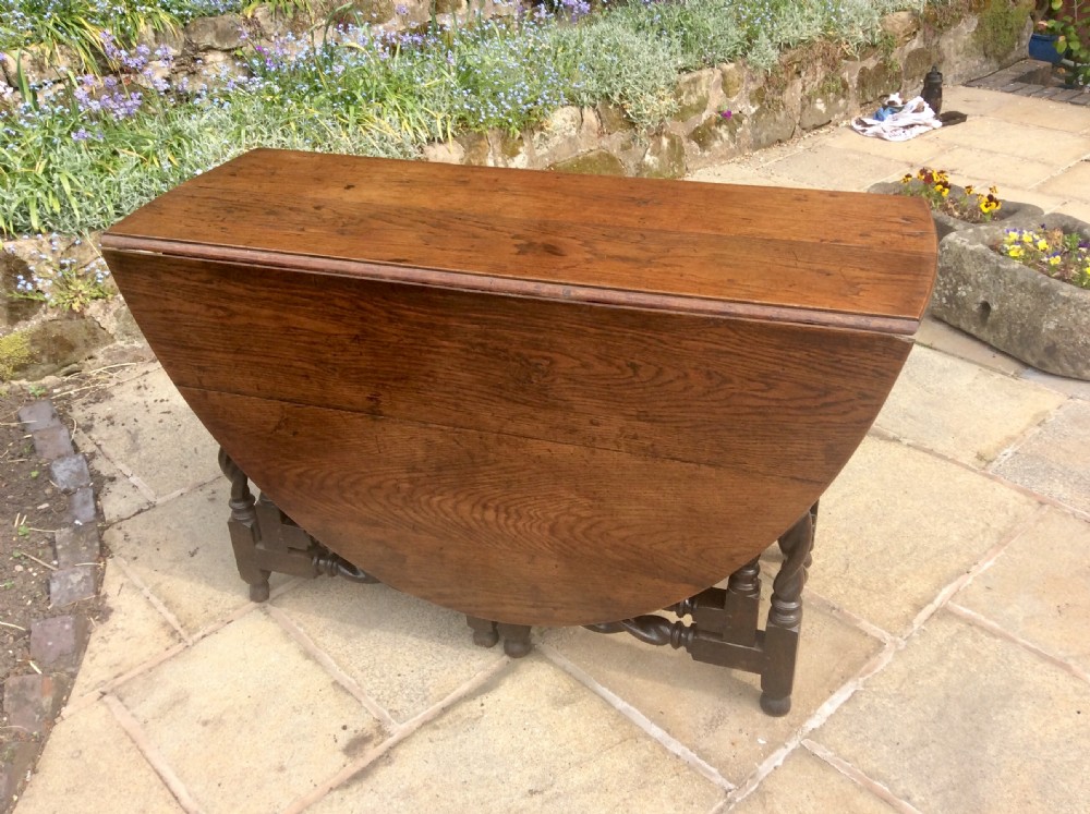 An antique dark oak oval gateleg table featuring barley twist turned legs, stretchers, and folding drop leaves. View IV