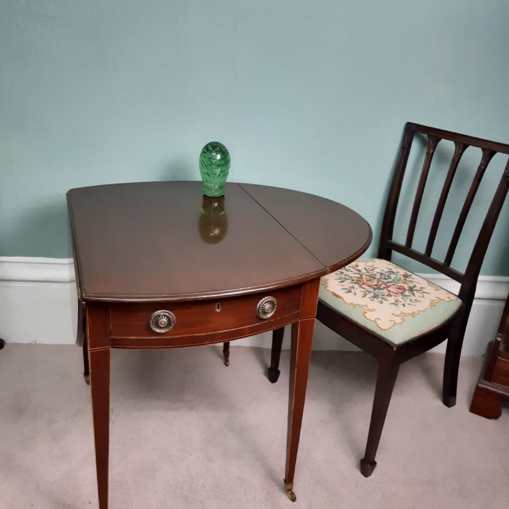 An 18th-century Georgian oval mahogany Pembroke table featuring two drop leaves, a single drawer with round brass handles, tapered legs, and brass castors. View II