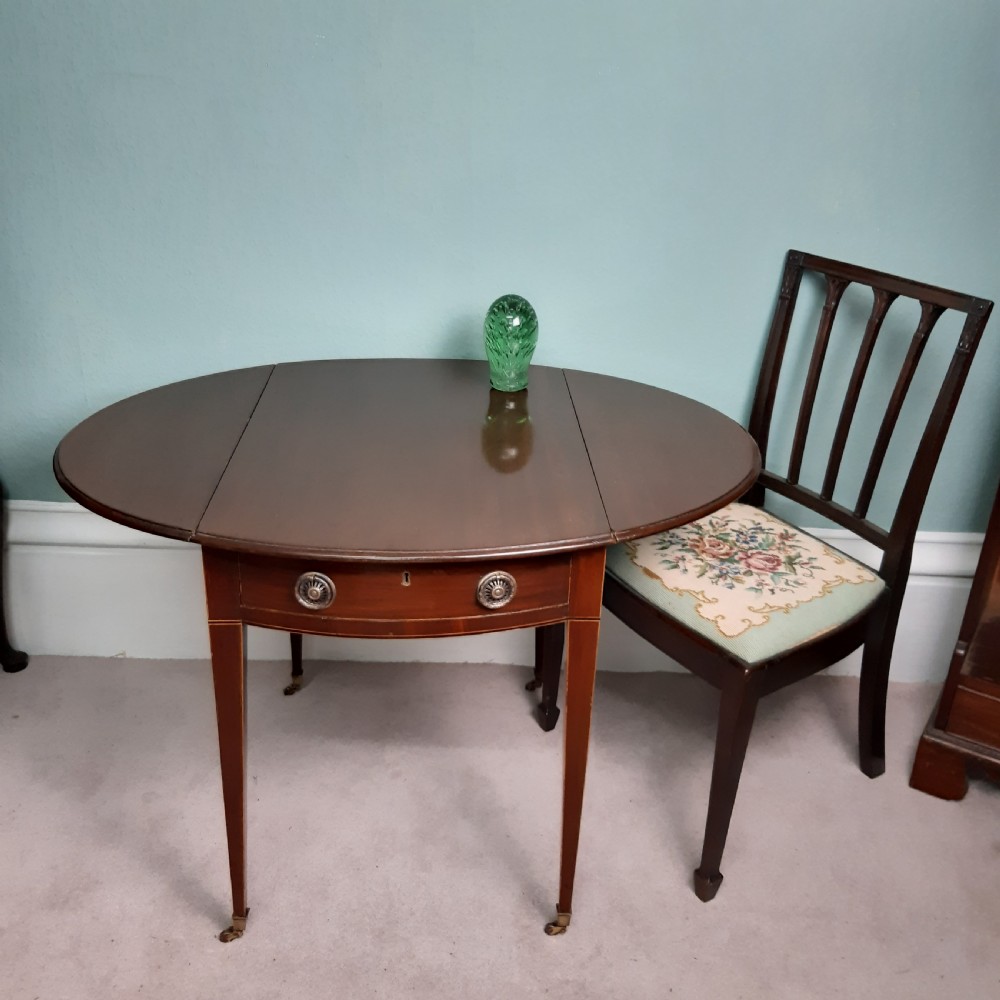 An 18th-century Georgian oval mahogany Pembroke table featuring two drop leaves, a single drawer with round brass handles, tapered legs, and brass castors. View III