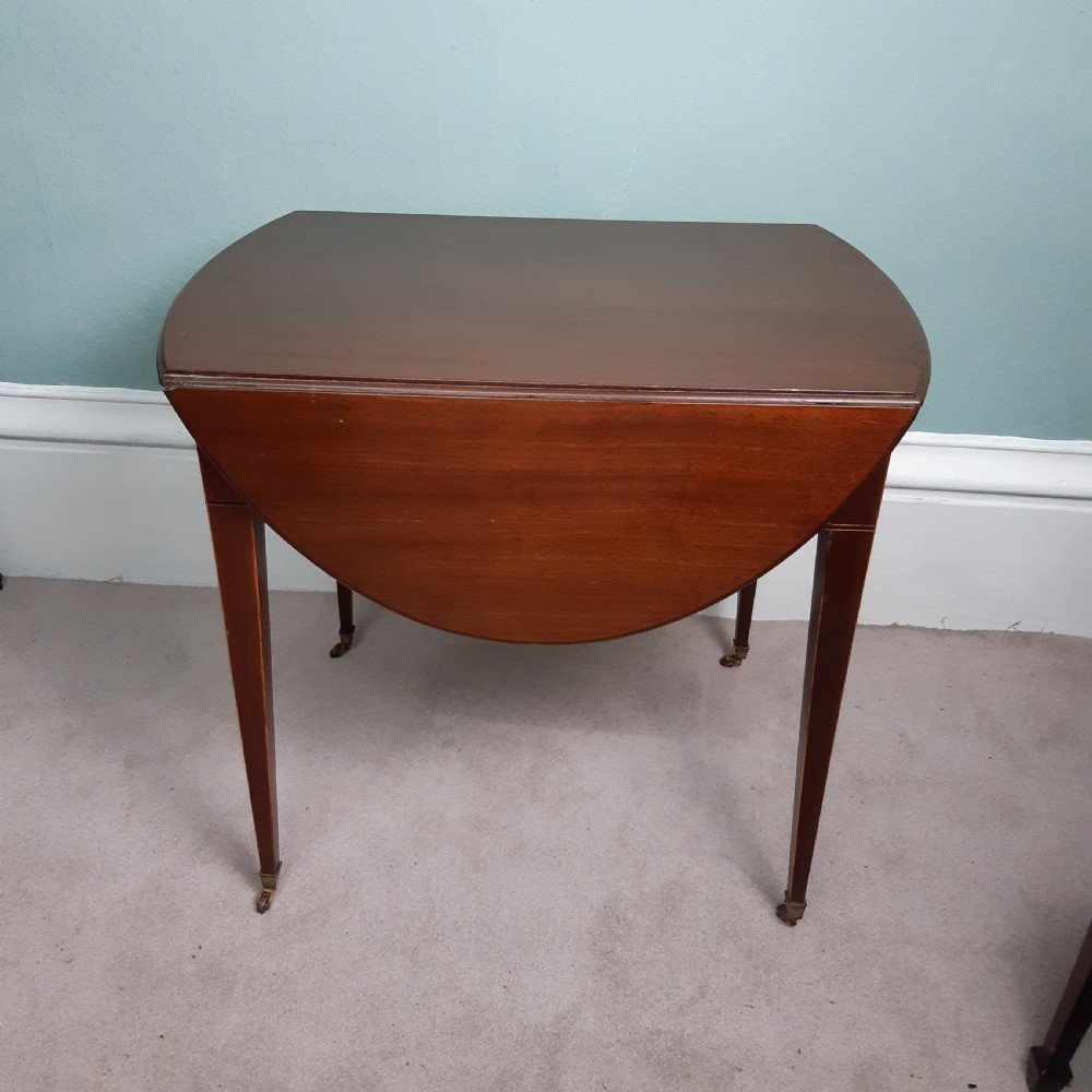 An 18th-century Georgian oval mahogany Pembroke table featuring two drop leaves, a single drawer with round brass handles, tapered legs, and brass castors. View IV