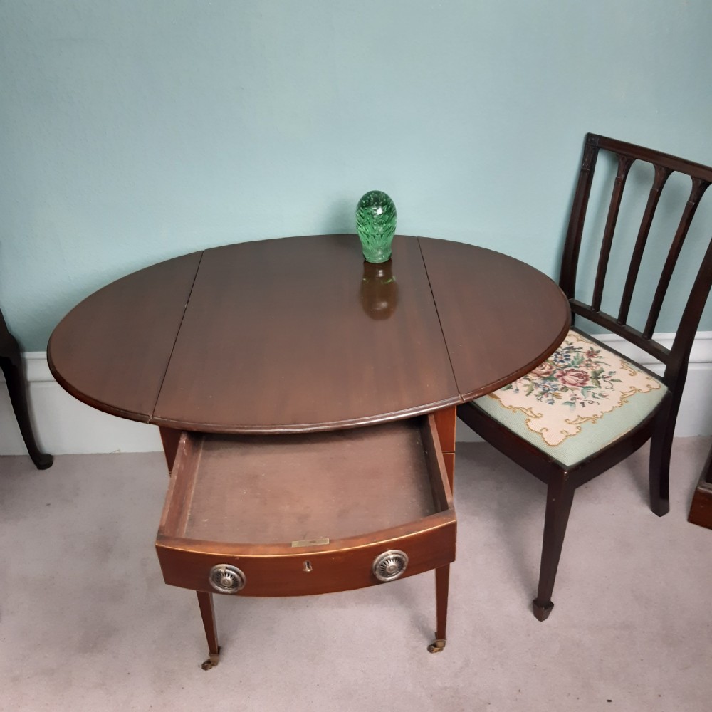 An 18th-century Georgian oval mahogany Pembroke table featuring two drop leaves, a single drawer with round brass handles, tapered legs, and brass castors. View V