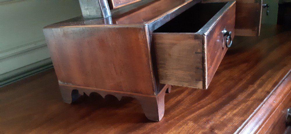 An antique Regency mahogany toilet mirror featuring an arched tilting mirror frame mounted on uprights over a two-drawer base with shell inlay. View VI