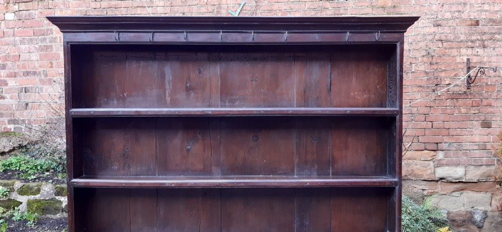 A dark oak antique dresser featuring an open plate rack with three shelves above three frieze drawers, supported by turned pillars over an open potboard base. View VIII