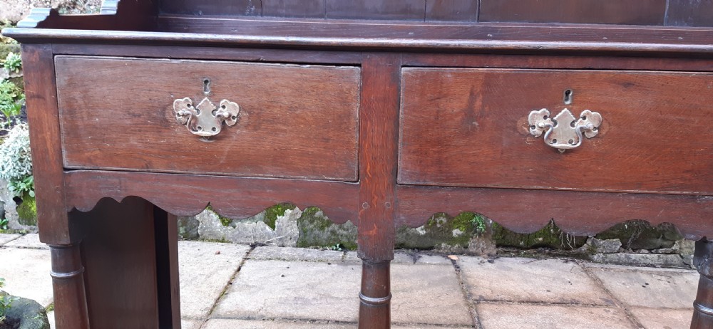 A dark oak antique dresser featuring an open plate rack with three shelves above three frieze drawers, supported by turned pillars over an open potboard base. View XII