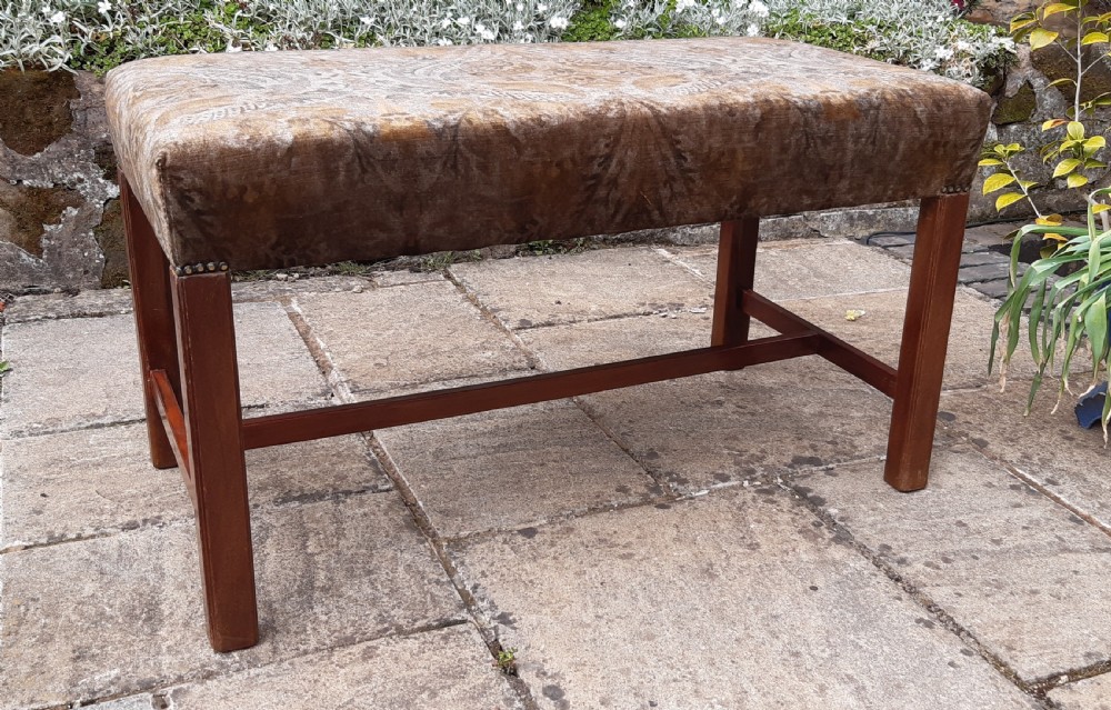 An upholstered rectangular mahogany stool featuring patterned brown fabric with stud detailing and straight legs joined by an H-stretcher.