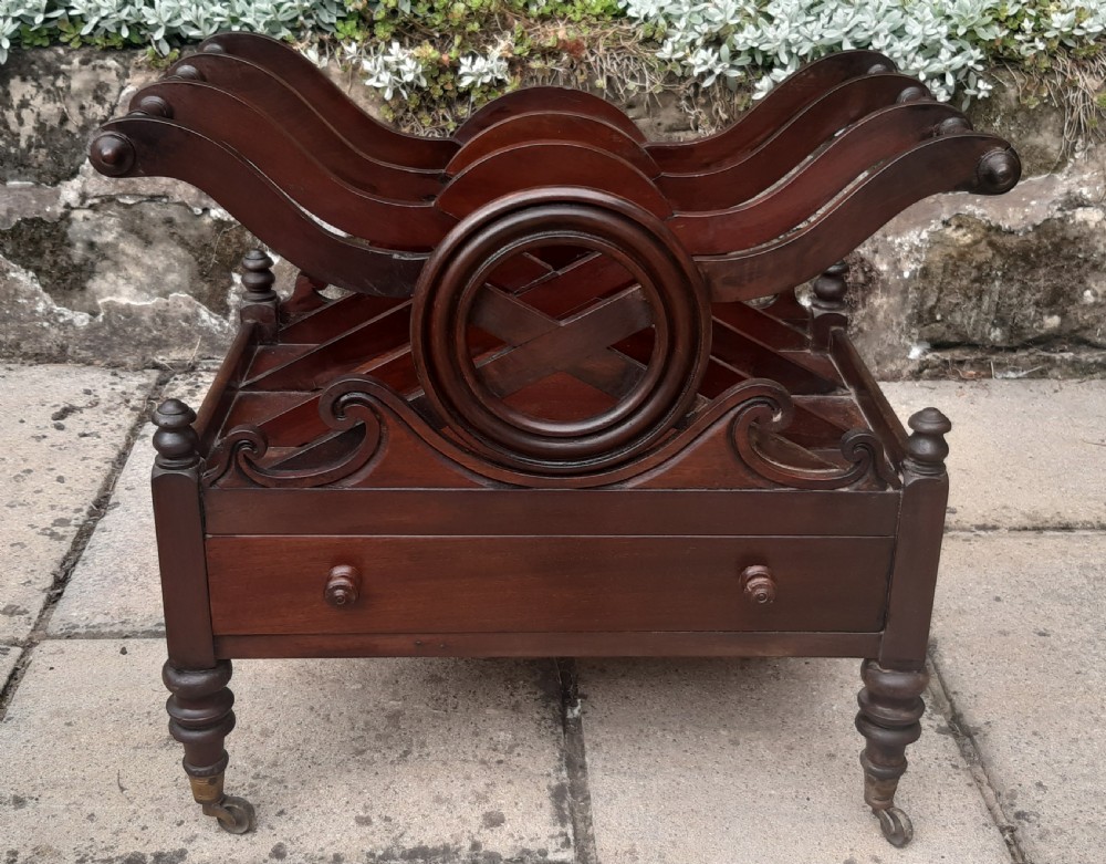 An early nineteenth-century mahogany Canterbury with curved slatted compartments, a central carved circular motif, a single drawer, and turned legs on brass castors.