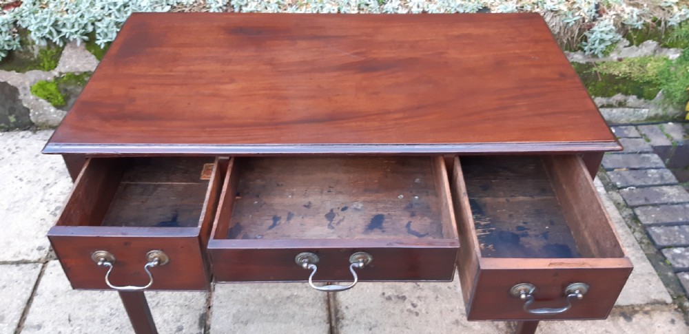 An antique Georgian dark mahogany lowboy featuring a rectangular top, three drawers with brass swan-neck handles, a shaped apron, and straight square legs. View VI