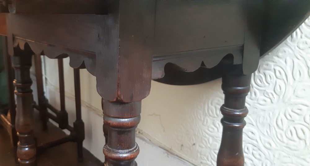 A dark brown oak drop-leaf occasional table featuring an oval top, turned baluster legs, and a rectangular box stretcher base. View XI