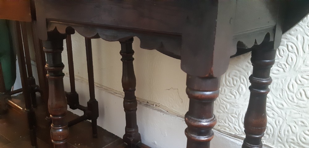 A dark brown oak drop-leaf occasional table featuring an oval top, turned baluster legs, and a rectangular box stretcher base. View XII