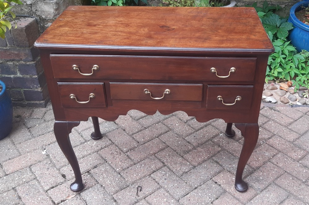 An Early Georgian mahogany lowboy featuring one wide upper drawer above three smaller drawers, brass swan-neck handles, a shaped lower apron, and cabriole legs with pad feet.