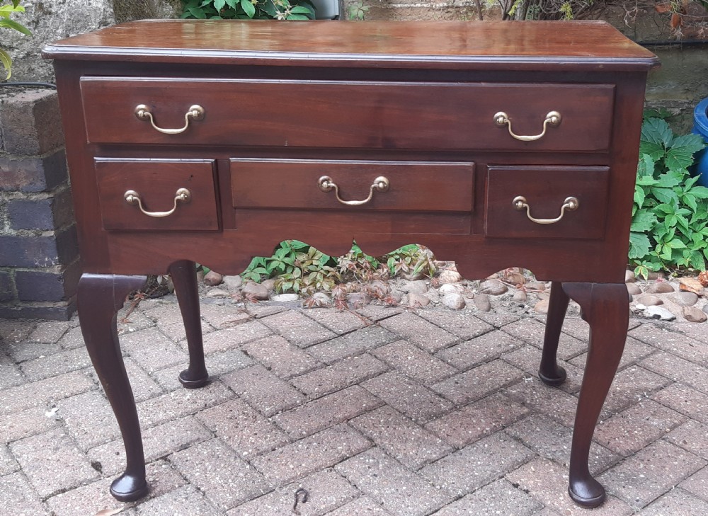 An Early Georgian mahogany lowboy featuring one wide upper drawer above three smaller drawers, brass swan-neck handles, a shaped lower apron, and cabriole legs with pad feet. View II