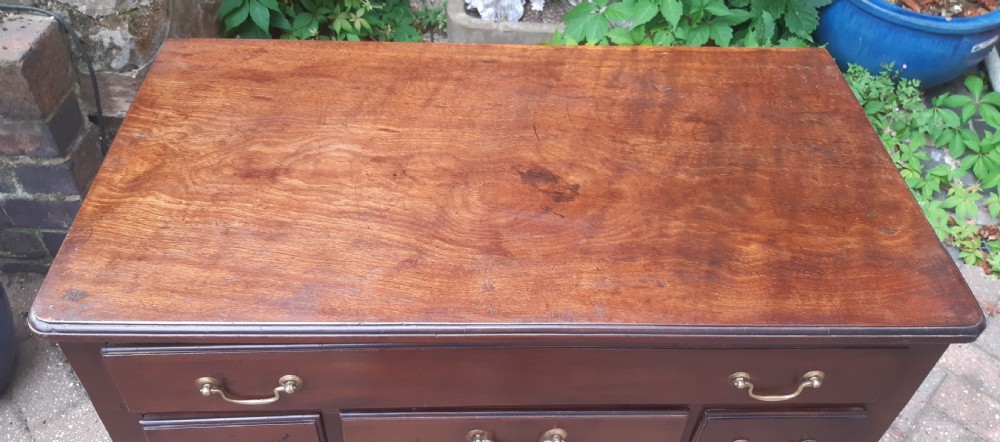 An Early Georgian mahogany lowboy featuring one wide upper drawer above three smaller drawers, brass swan-neck handles, a shaped lower apron, and cabriole legs with pad feet. View IV