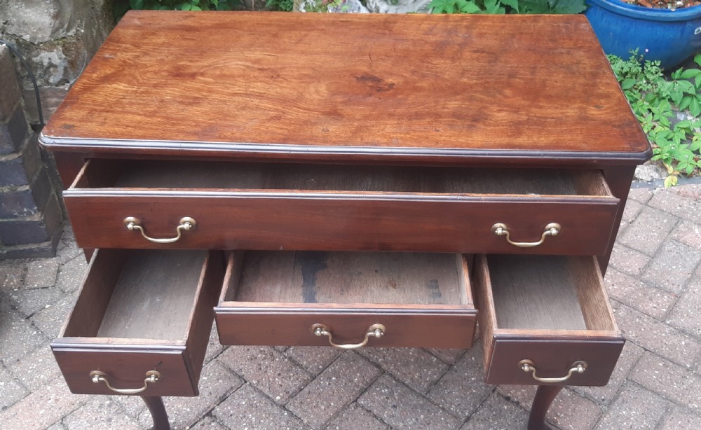 An Early Georgian mahogany lowboy featuring one wide upper drawer above three smaller drawers, brass swan-neck handles, a shaped lower apron, and cabriole legs with pad feet. View VII