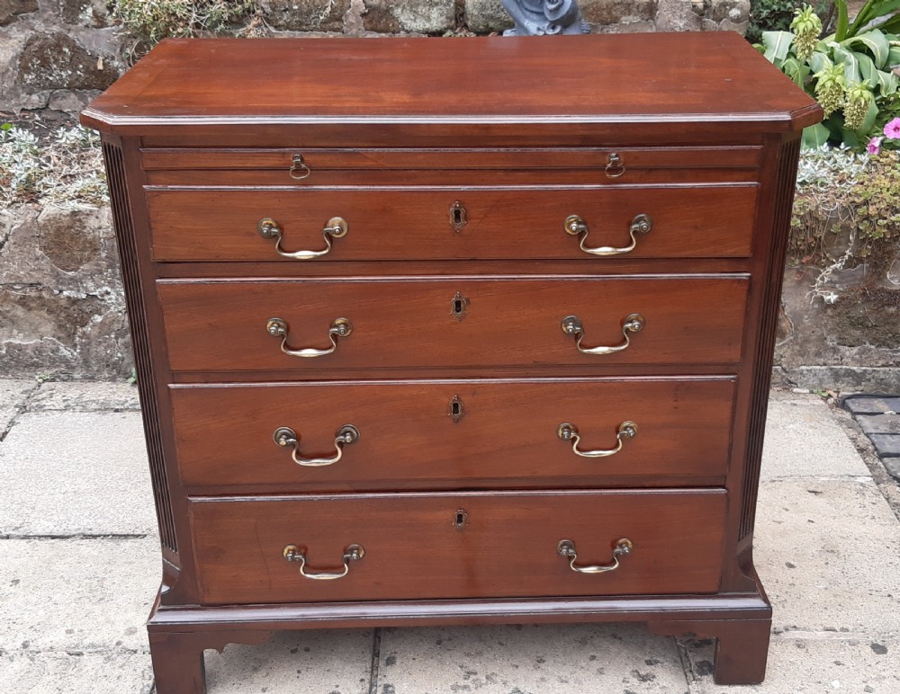 A small Georgian mahogany chest of drawers featuring four graduated drawers with brass handles, a pull-out brushing slide, canted reeded corners, and bracket feet.