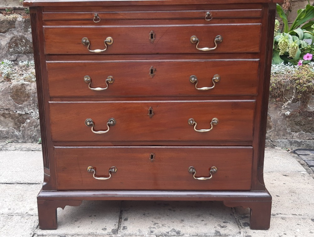 A small Georgian mahogany chest of drawers featuring four graduated drawers with brass handles, a pull-out brushing slide, canted reeded corners, and bracket feet. View II