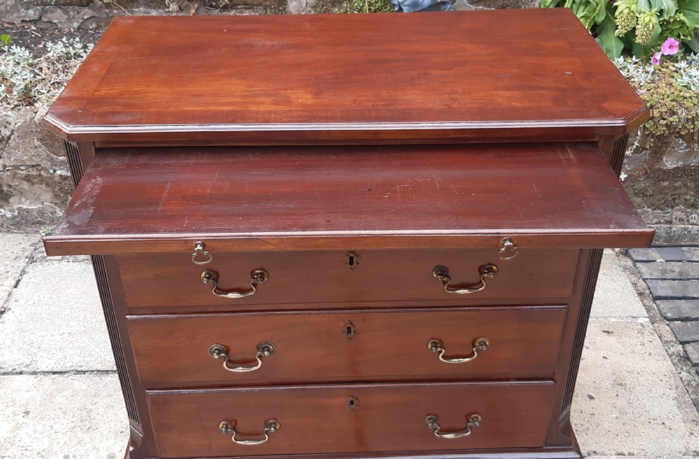 A small Georgian mahogany chest of drawers featuring four graduated drawers with brass handles, a pull-out brushing slide, canted reeded corners, and bracket feet. View V