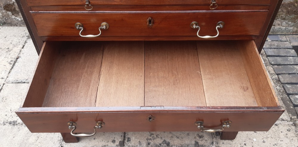 A small Georgian mahogany chest of drawers featuring four graduated drawers with brass handles, a pull-out brushing slide, canted reeded corners, and bracket feet. View VII