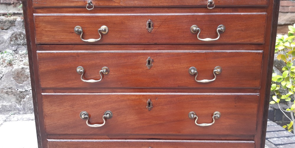 A small Georgian mahogany chest of drawers featuring four graduated drawers with brass handles, a pull-out brushing slide, canted reeded corners, and bracket feet. View XII
