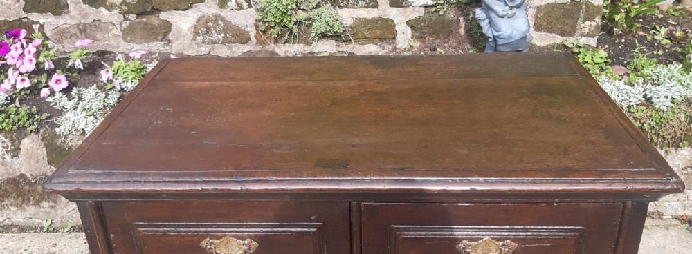 A 17th-century dark oak chest of drawers featuring geometric panelled drawer fronts, brass drop handles, keyhole escutcheons, and turned bun feet. View III