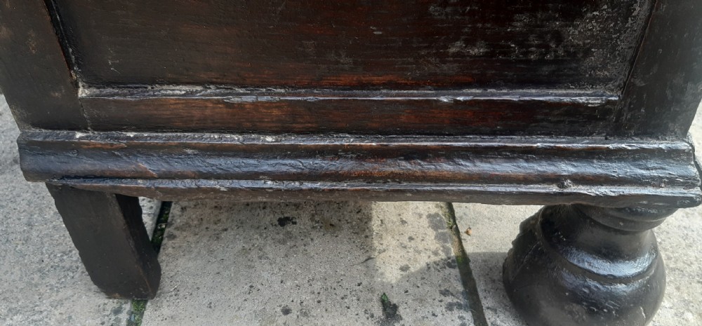 A 17th-century dark oak chest of drawers featuring geometric panelled drawer fronts, brass drop handles, keyhole escutcheons, and turned bun feet. View XI