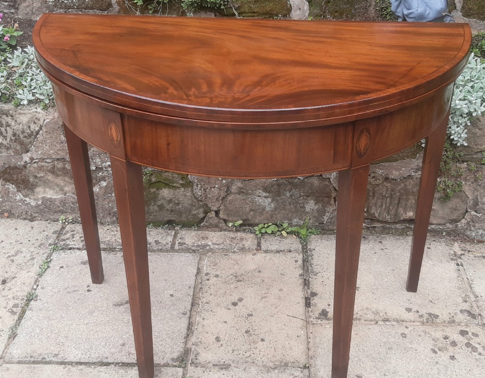 A semicircular Georgian mahogany demi lune card table featuring figured wood grain and tapering legs.
