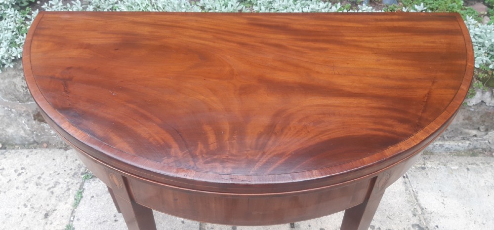 A semicircular Georgian mahogany demi lune card table featuring figured wood grain and tapering legs. View II