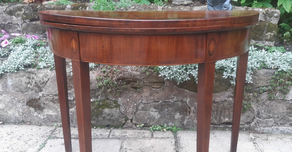 A semicircular Georgian mahogany demi lune card table featuring figured wood grain and tapering legs. View III