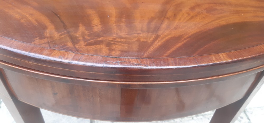 A semicircular Georgian mahogany demi lune card table featuring figured wood grain and tapering legs. View VII