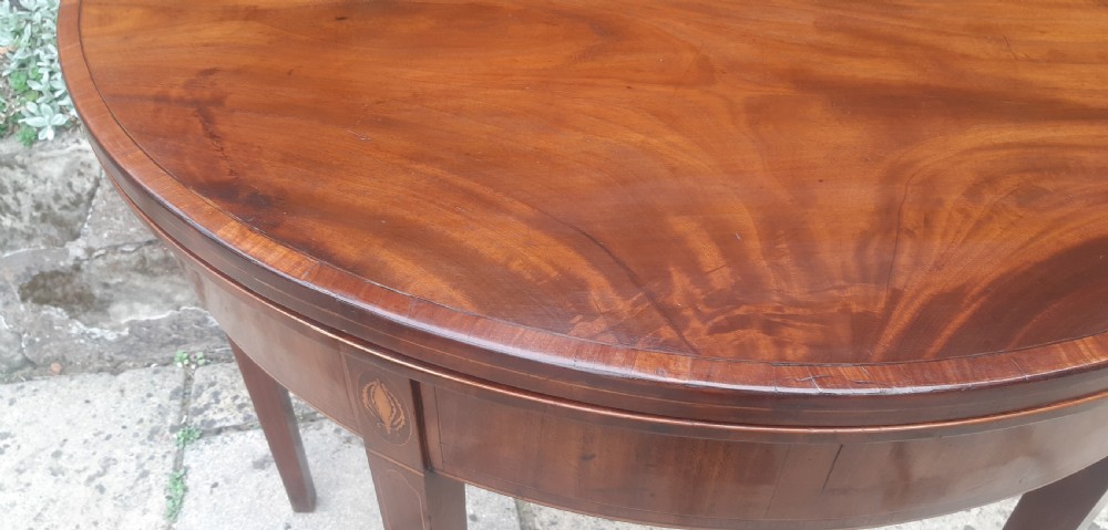 A semicircular Georgian mahogany demi lune card table featuring figured wood grain and tapering legs. View VIII