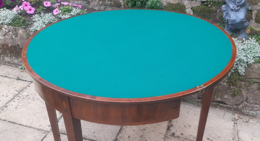A semicircular Georgian mahogany demi lune card table featuring figured wood grain and tapering legs. View X