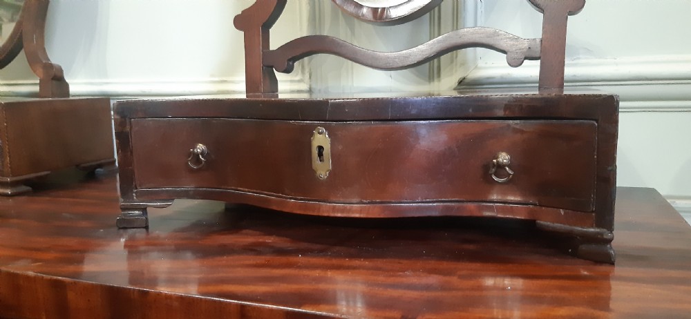 An antique mahogany toilet mirror featuring an adjustable swivel glass frame held by curved uprights above a serpentine drawer base with brass hardware. View III