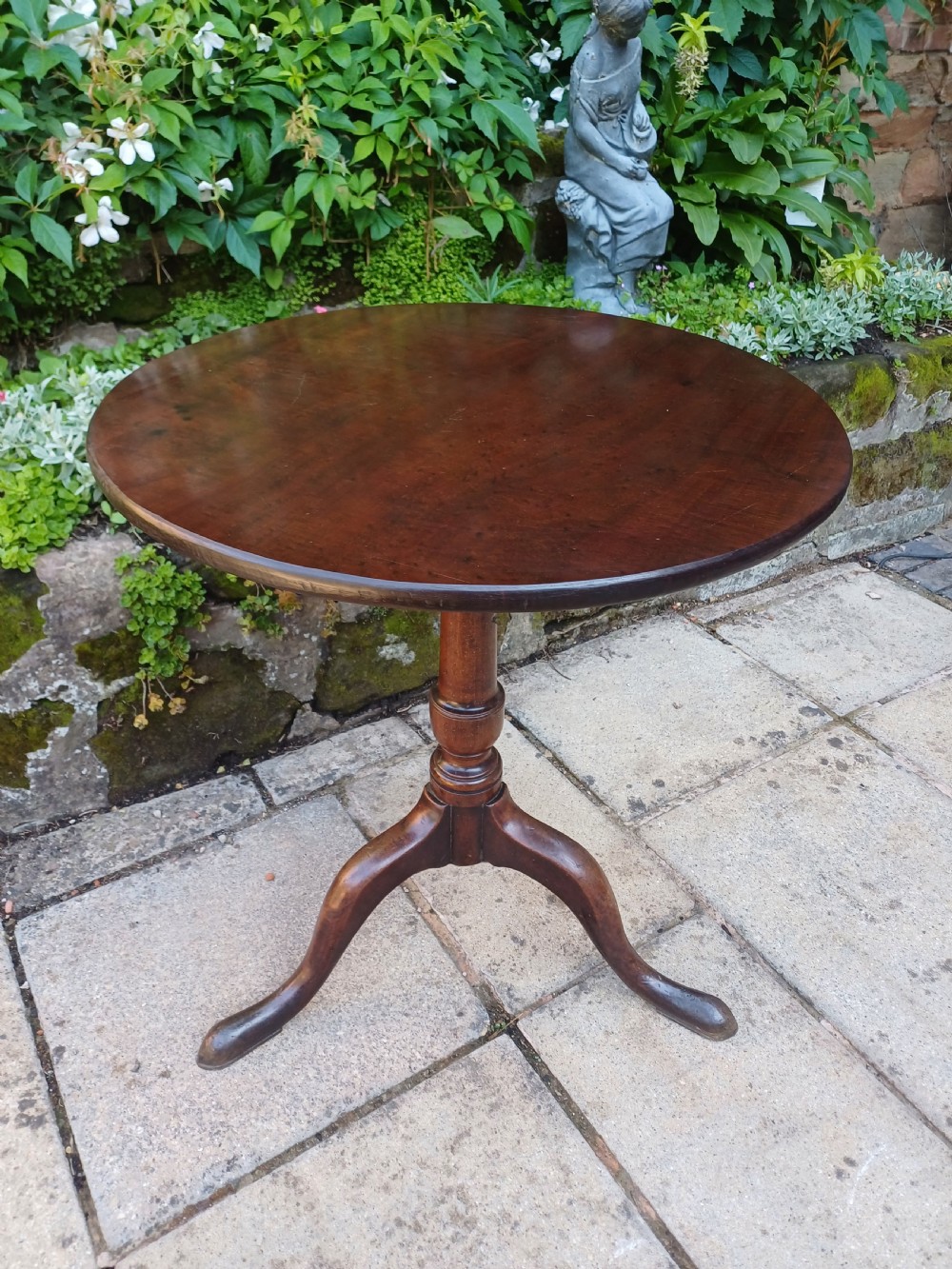 A Georgian mahogany tripod table featuring a circular top, a turned central baluster pedestal, and three splayed cabriole legs.