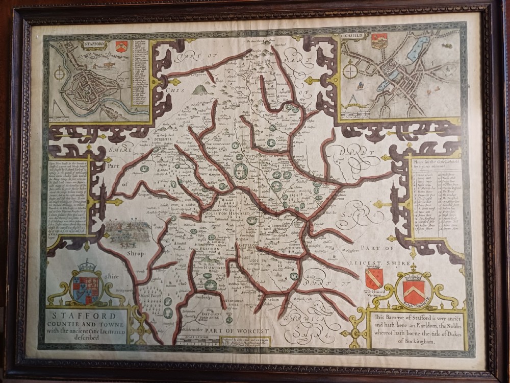 Framed 17th-century hand-coloured engraved map of Staffordshire by John Speed featuring heraldic crests and inset town plans of Stafford and Lichfield.