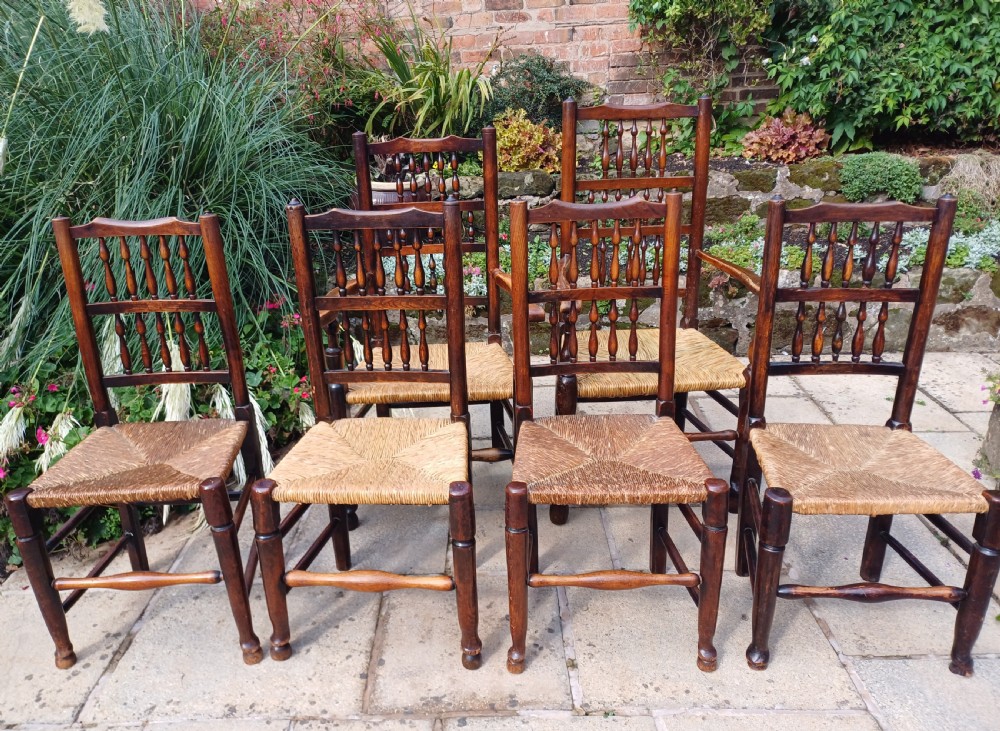 A set of six dark oak spindleback dining chairs featuring hand-woven rush seats and turned wooden legs.